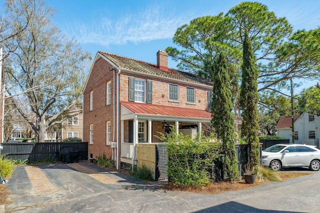 view of front facade featuring a porch, brick siding, a fenced front yard, and a chimney