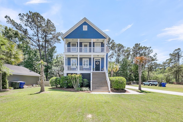 coastal inspired home with a balcony, a porch, stairway, and a front yard
