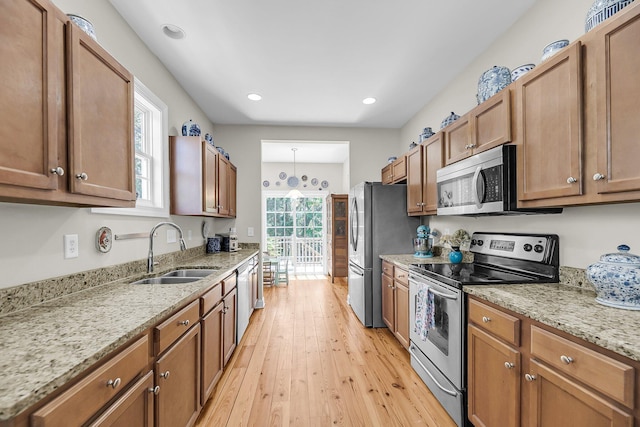 kitchen with appliances with stainless steel finishes, light stone countertops, brown cabinets, light wood-type flooring, and a sink