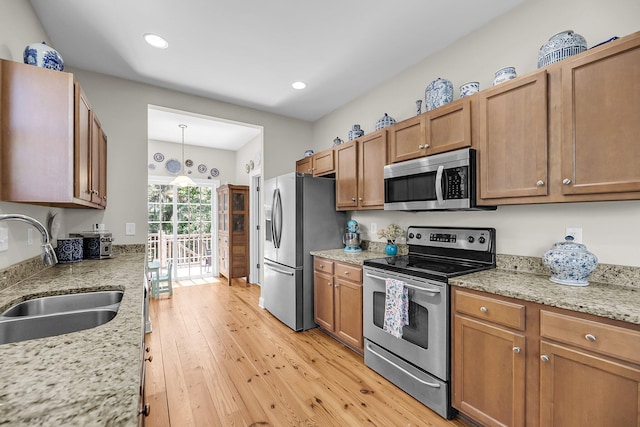 kitchen featuring light stone countertops, brown cabinets, a sink, light wood-style flooring, and appliances with stainless steel finishes