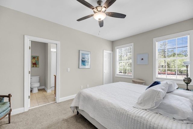 bedroom featuring baseboards, light colored carpet, ceiling fan, and ensuite bath