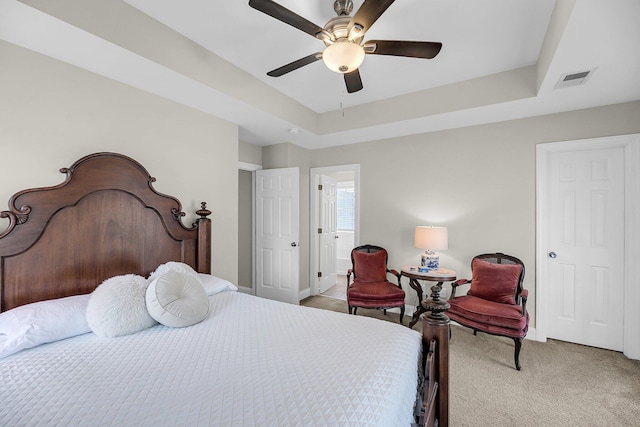 bedroom with visible vents, light carpet, baseboards, a tray ceiling, and a ceiling fan