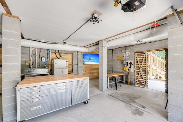 below grade area featuring freestanding refrigerator and concrete block wall