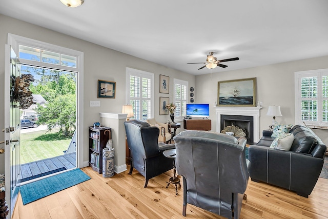living room with a ceiling fan, baseboards, light wood finished floors, and a fireplace