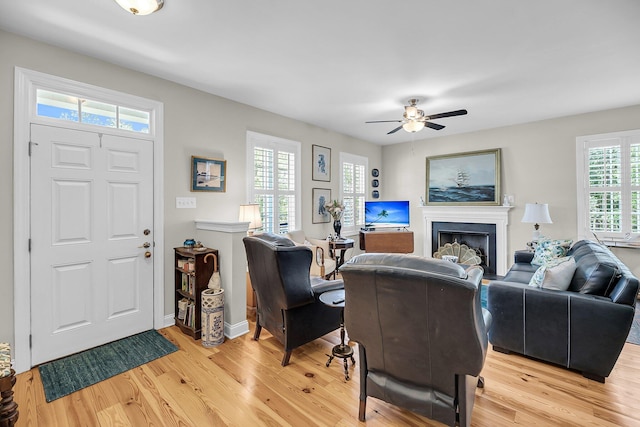 living area featuring light wood-style floors, baseboards, ceiling fan, and a fireplace