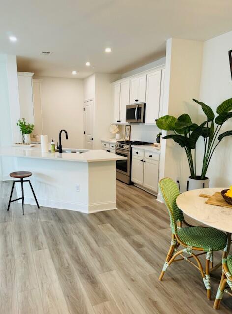 kitchen with a kitchen breakfast bar, stainless steel appliances, light hardwood / wood-style floors, sink, and white cabinetry