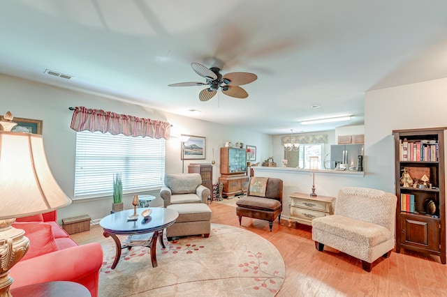 living room featuring ceiling fan with notable chandelier and light hardwood / wood-style flooring