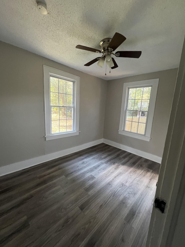 empty room with dark wood finished floors, plenty of natural light, baseboards, and a textured ceiling