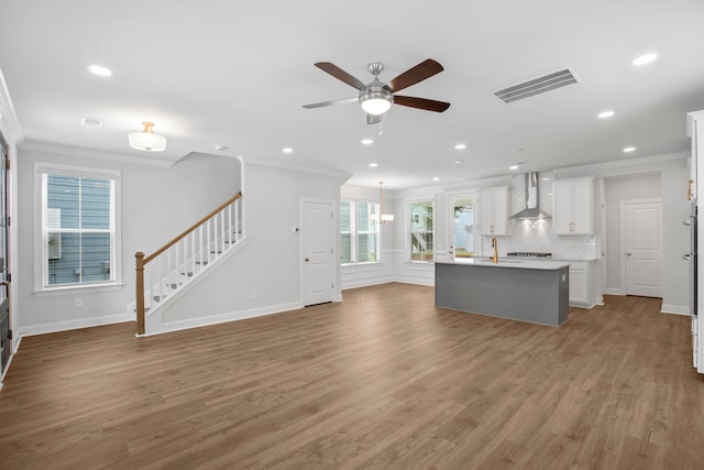 unfurnished living room featuring crown molding, sink, ceiling fan with notable chandelier, and light wood-type flooring