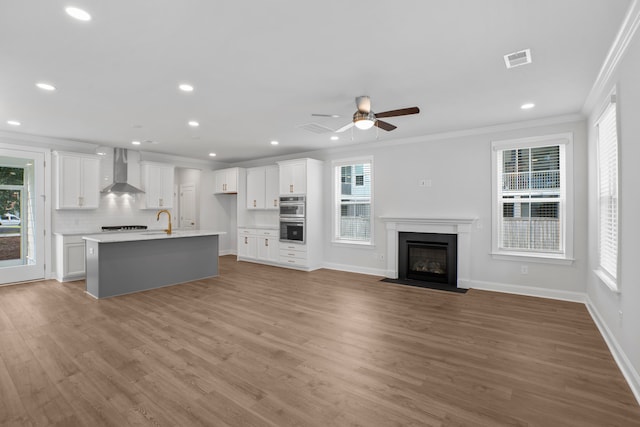 unfurnished living room featuring crown molding, sink, ceiling fan, and light wood-type flooring