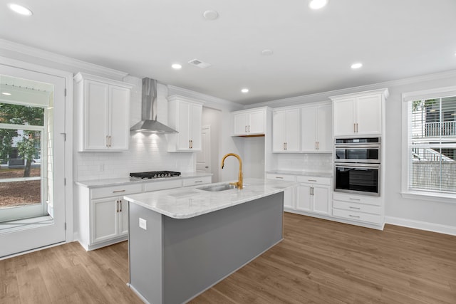 kitchen featuring a center island with sink, wall chimney exhaust hood, white cabinetry, and sink