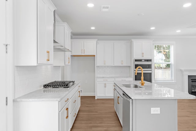 kitchen featuring white cabinetry, stainless steel appliances, ornamental molding, an island with sink, and light wood-type flooring