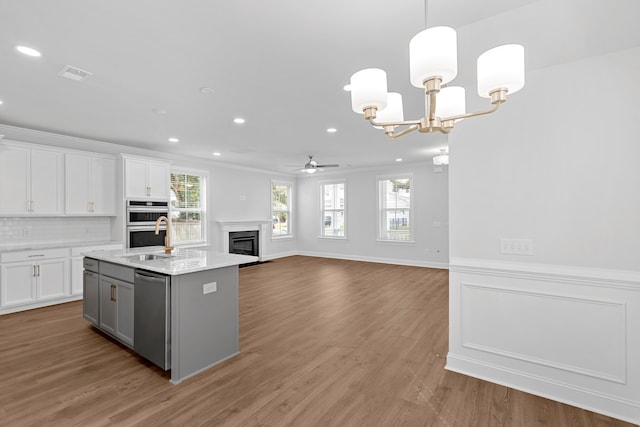 kitchen with stainless steel appliances, crown molding, wood-type flooring, a center island with sink, and white cabinetry