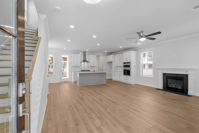 unfurnished living room with ceiling fan, plenty of natural light, light hardwood / wood-style floors, and ornamental molding