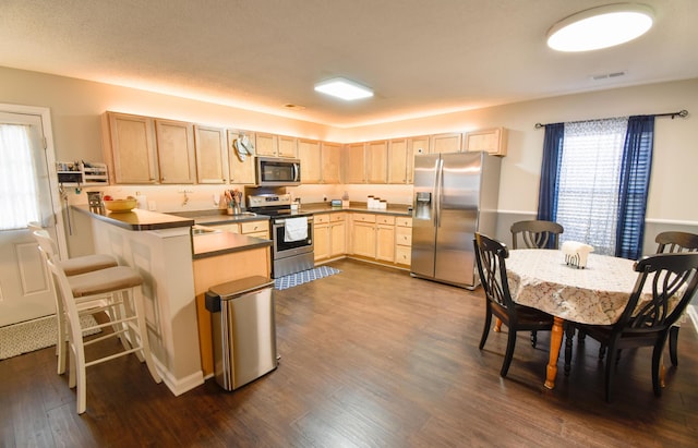 kitchen featuring dark wood-style flooring, visible vents, appliances with stainless steel finishes, light brown cabinets, and a peninsula