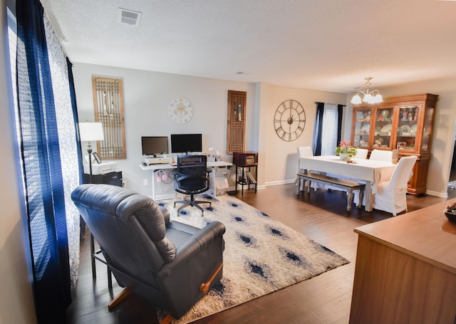 living room with a chandelier, a textured ceiling, wood finished floors, visible vents, and baseboards