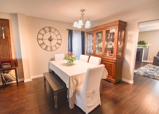 dining room with dark wood finished floors, a textured ceiling, baseboards, and an inviting chandelier