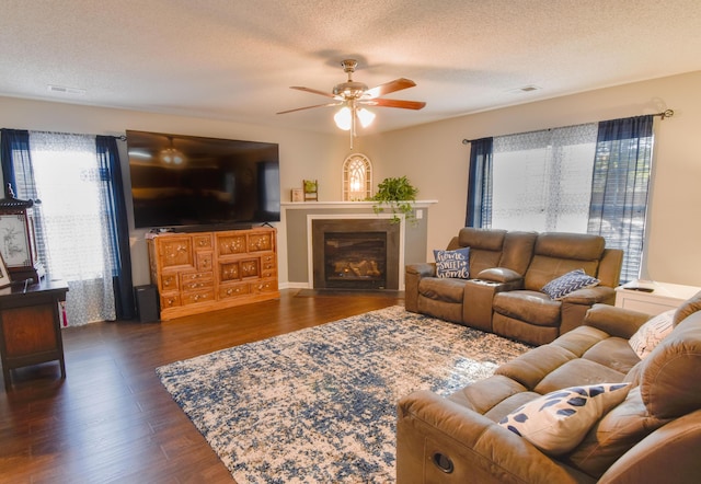 living area with dark wood-style floors, a textured ceiling, a glass covered fireplace, and a ceiling fan