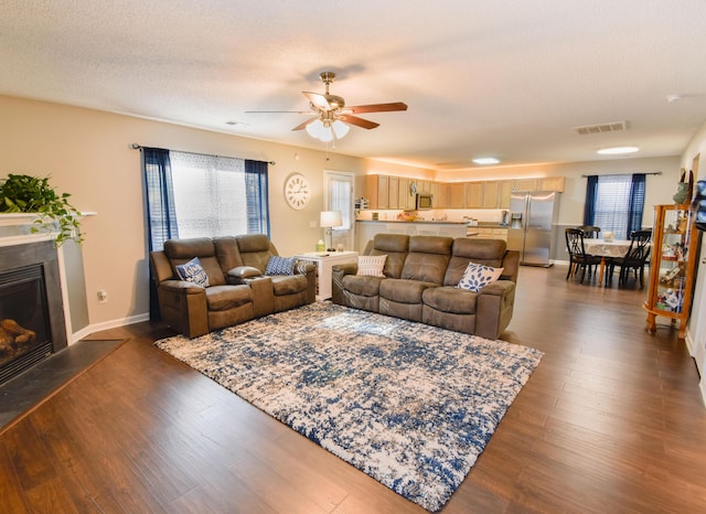 living room with dark wood-style floors, a glass covered fireplace, visible vents, and plenty of natural light