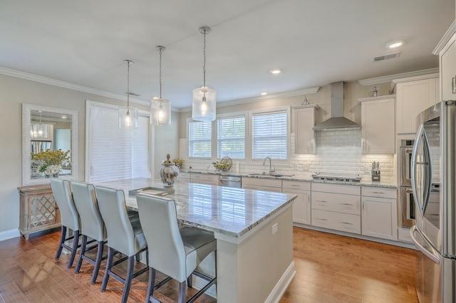 kitchen with appliances with stainless steel finishes, a kitchen island, wall chimney exhaust hood, and white cabinets