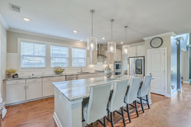 kitchen featuring wall chimney range hood, light wood-type flooring, pendant lighting, a kitchen island, and white cabinets