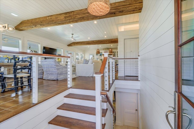 stairs with ceiling fan, beamed ceiling, and wooden walls