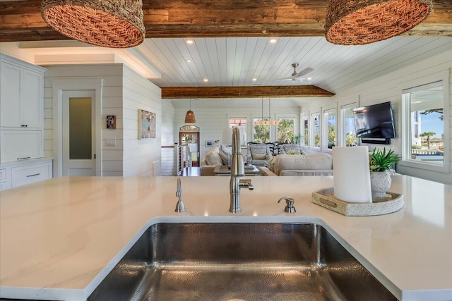 kitchen with light stone countertops, wooden walls, sink, ceiling fan, and beam ceiling