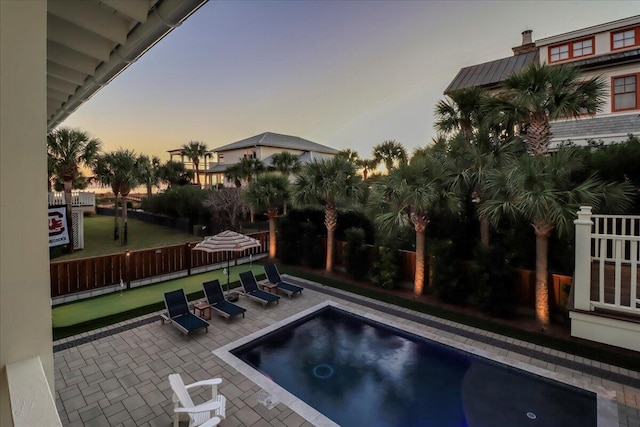 pool at dusk with a hot tub and a patio area