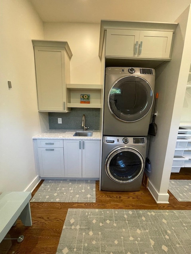 laundry area with stacked washer and dryer, dark hardwood / wood-style floors, sink, and cabinets