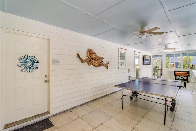 recreation room with ceiling fan, light tile patterned floors, and wood walls