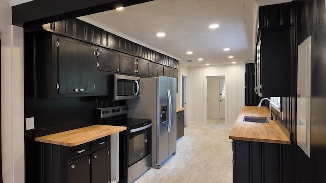 kitchen with sink, butcher block countertops, crown molding, appliances with stainless steel finishes, and light wood-type flooring