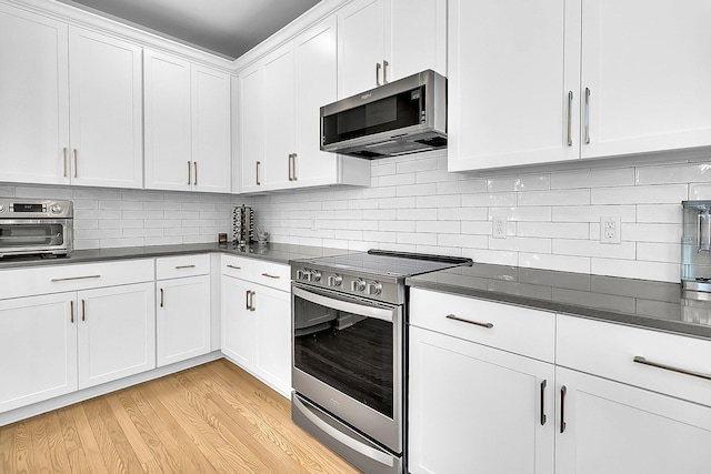 kitchen with tasteful backsplash, white cabinets, appliances with stainless steel finishes, and light hardwood / wood-style flooring