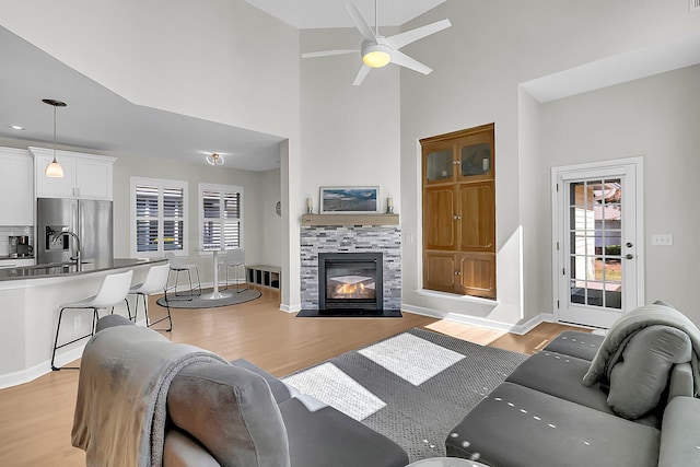 living room featuring ceiling fan, light hardwood / wood-style flooring, a tile fireplace, and high vaulted ceiling