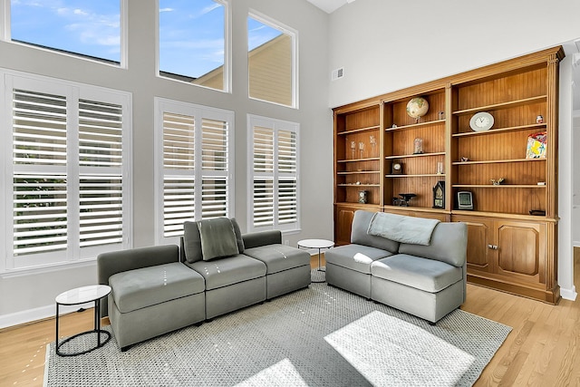 living room featuring plenty of natural light, light hardwood / wood-style flooring, and a towering ceiling