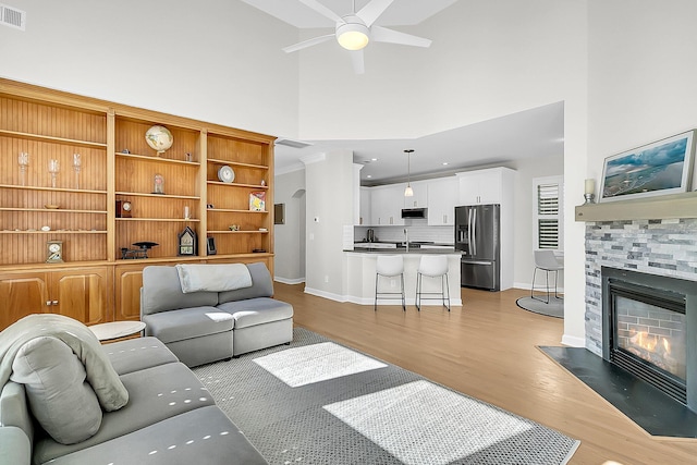 living room featuring ceiling fan, a fireplace, light hardwood / wood-style floors, a towering ceiling, and sink