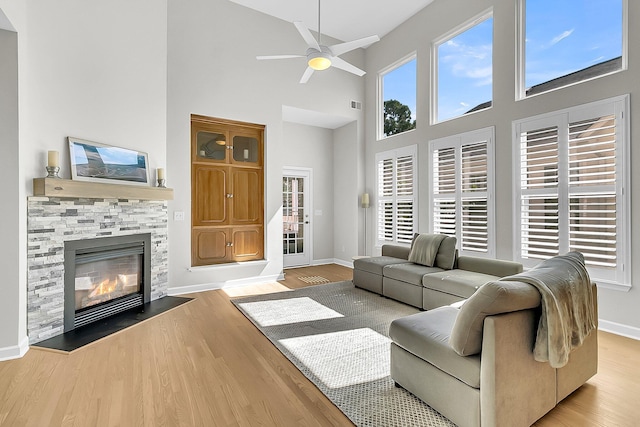 living room featuring a towering ceiling, ceiling fan, a fireplace, and light hardwood / wood-style flooring