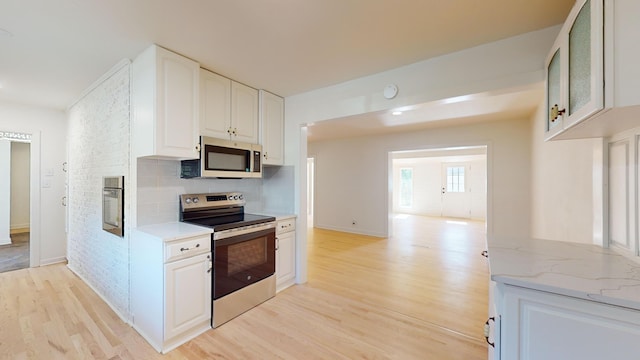 kitchen featuring light hardwood / wood-style flooring, white cabinetry, backsplash, stainless steel appliances, and light stone countertops