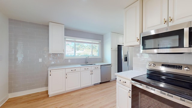 kitchen with sink, appliances with stainless steel finishes, white cabinets, light hardwood / wood-style floors, and backsplash