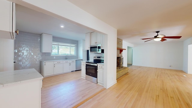 kitchen with sink, light hardwood / wood-style flooring, appliances with stainless steel finishes, white cabinets, and a brick fireplace