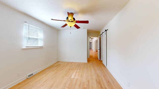 spare room with ceiling fan, a barn door, and light hardwood / wood-style flooring