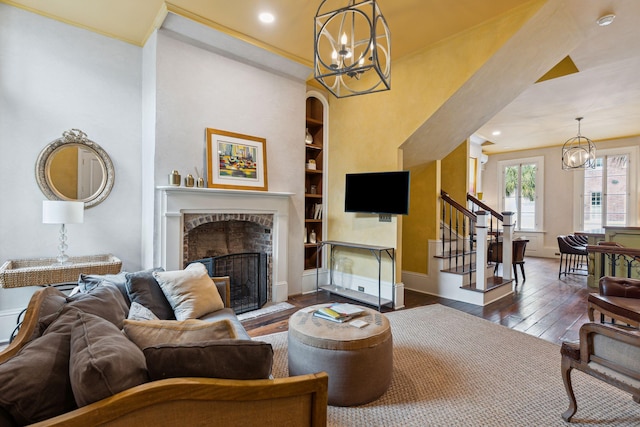 living room featuring crown molding, dark hardwood / wood-style floors, a brick fireplace, built in shelves, and a chandelier