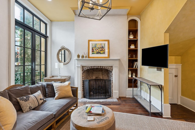 living room with crown molding, dark wood-type flooring, built in features, a notable chandelier, and a fireplace