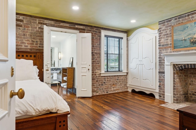 bedroom with brick wall, dark hardwood / wood-style flooring, and a brick fireplace