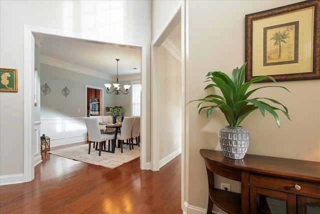 corridor with crown molding, dark wood-type flooring, and an inviting chandelier