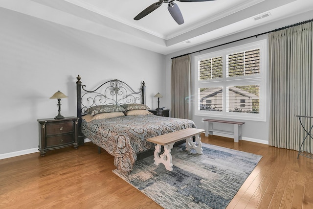 bedroom with ceiling fan, crown molding, wood-type flooring, and a tray ceiling