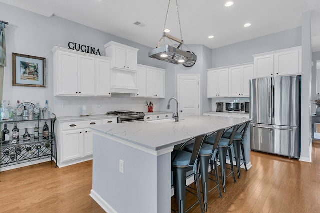 kitchen featuring premium range hood, white cabinets, appliances with stainless steel finishes, and a center island with sink