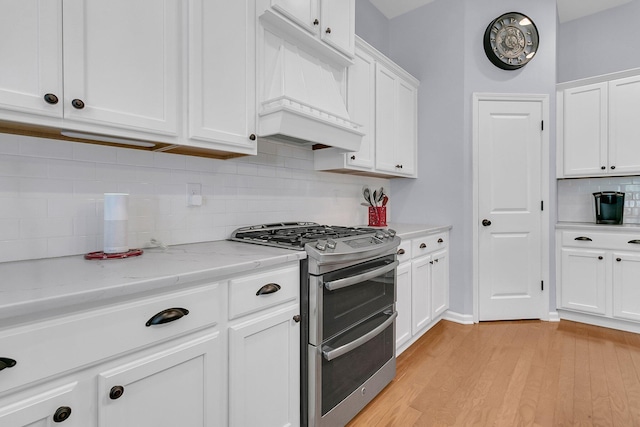 kitchen featuring double oven range, white cabinetry, custom exhaust hood, and light stone countertops