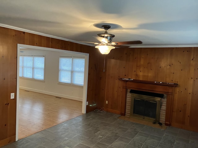 unfurnished living room featuring ceiling fan, crown molding, wooden walls, and a brick fireplace