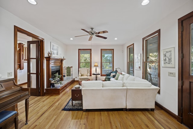 living room with light wood-style flooring, a ceiling fan, a fireplace with raised hearth, and recessed lighting