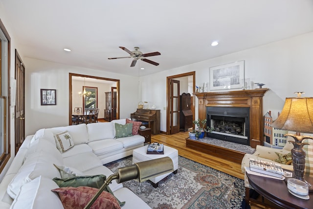 living area featuring a fireplace with flush hearth, wood finished floors, ceiling fan with notable chandelier, and recessed lighting